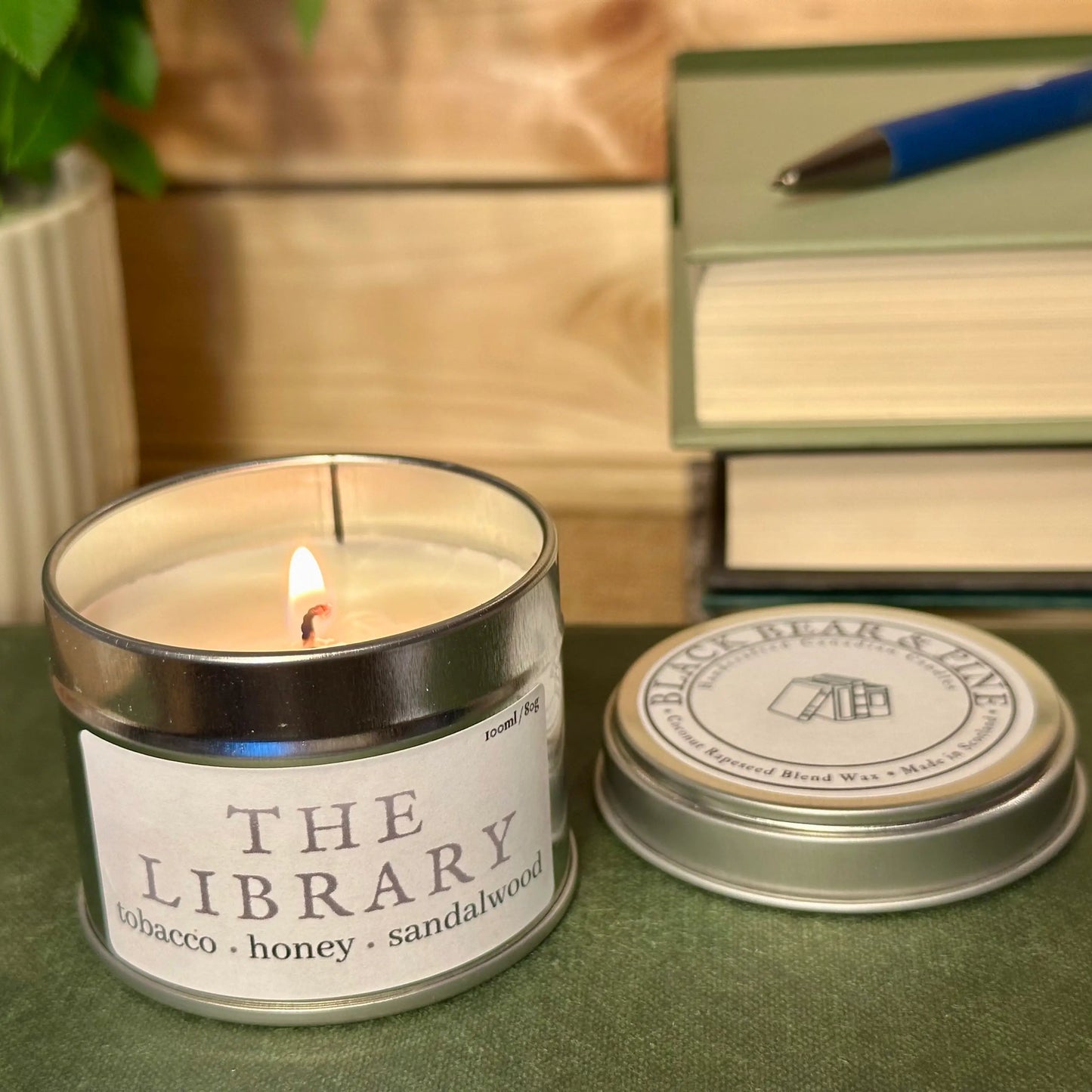 Candle labeled 'The Library' with a stack of books and pen in the background